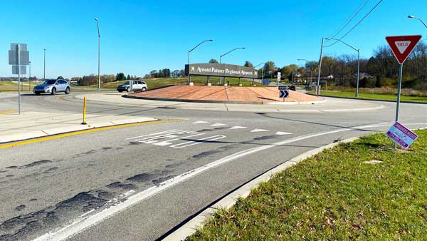 Cars driving a roundabout with a sign for the airport in center